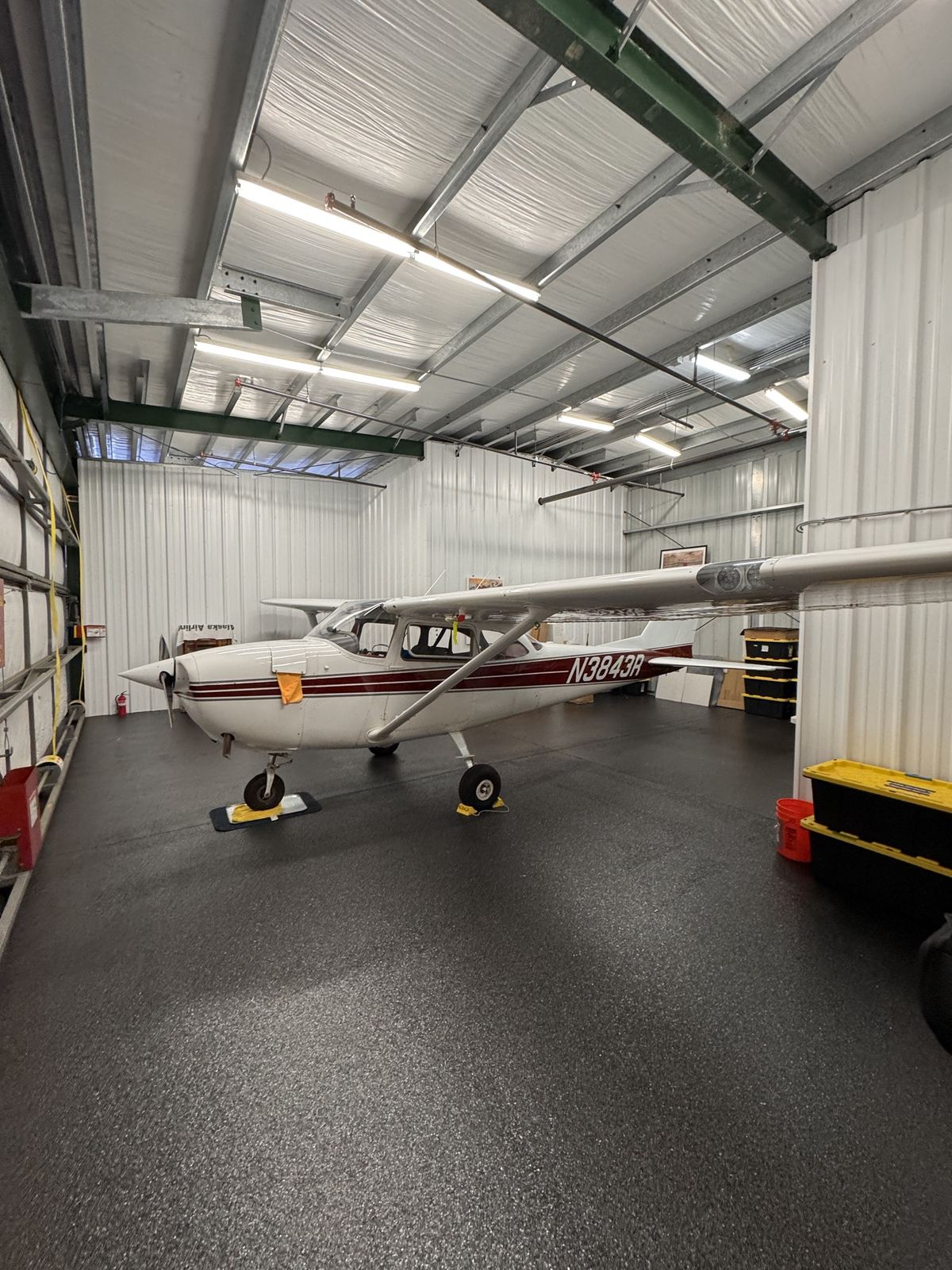 White Cessna 172 with a maroon stripe, tail number N3843R, parked in a clean, brightly lit hangar